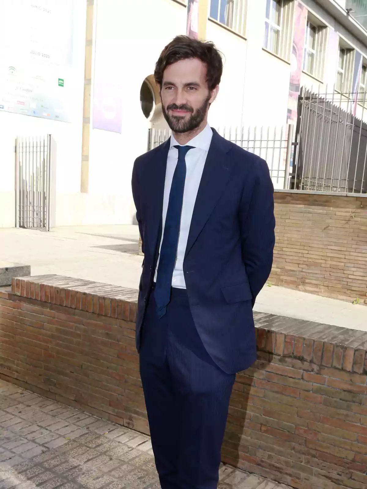 Un hombre con traje azul y corbata de pie al aire libre frente a un edificio. Un hombre con traje azul y corbata de pie al aire libre frente a un edificio.