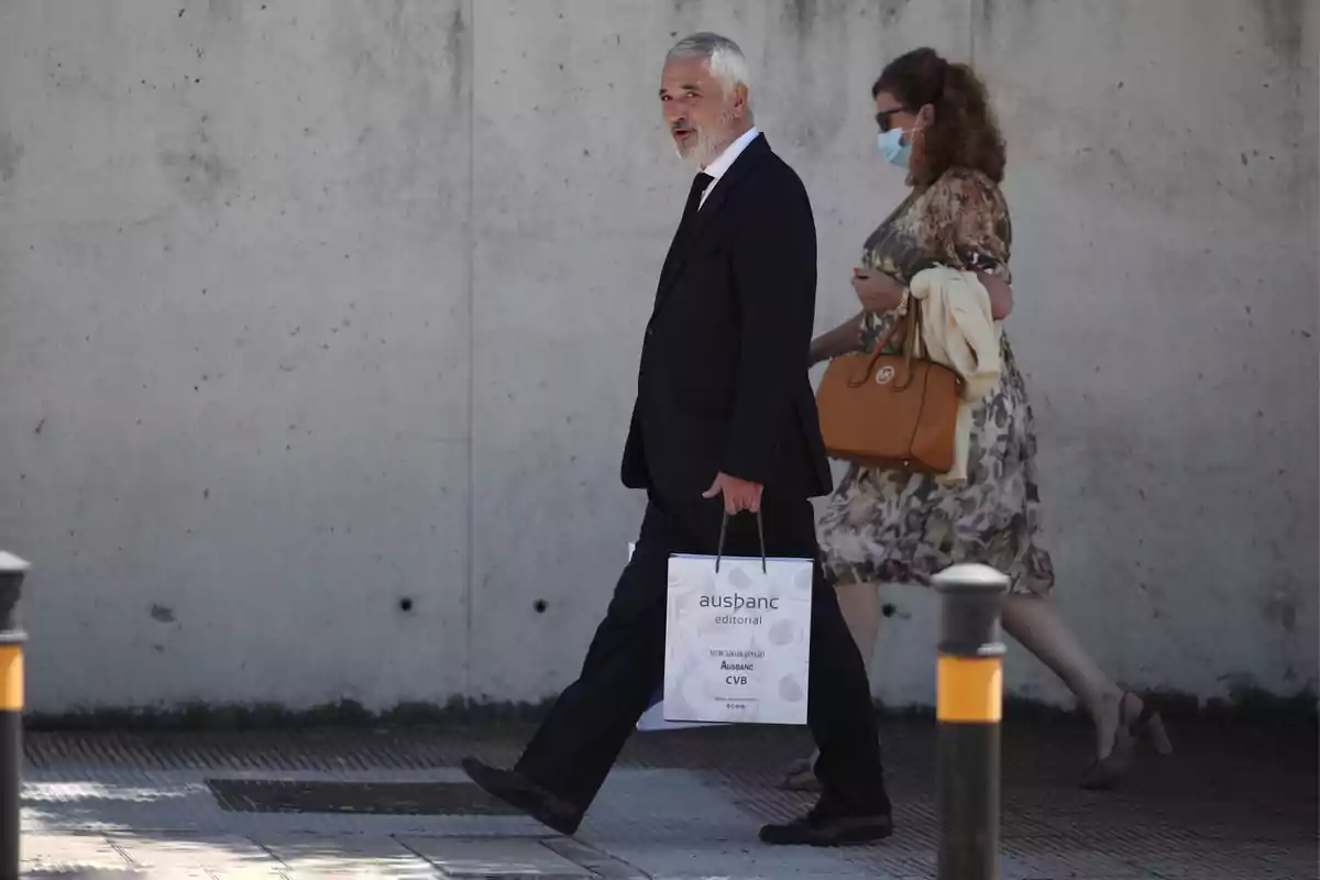 Dos personas caminando por la acera, una de ellas lleva una bolsa de papel y la otra un bolso grande.