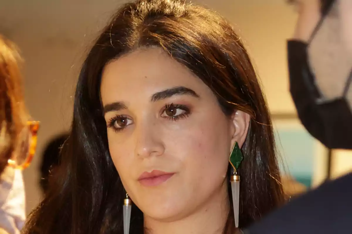 Mujer de cabello largo y oscuro con pendientes largos y expresión seria en un ambiente interior