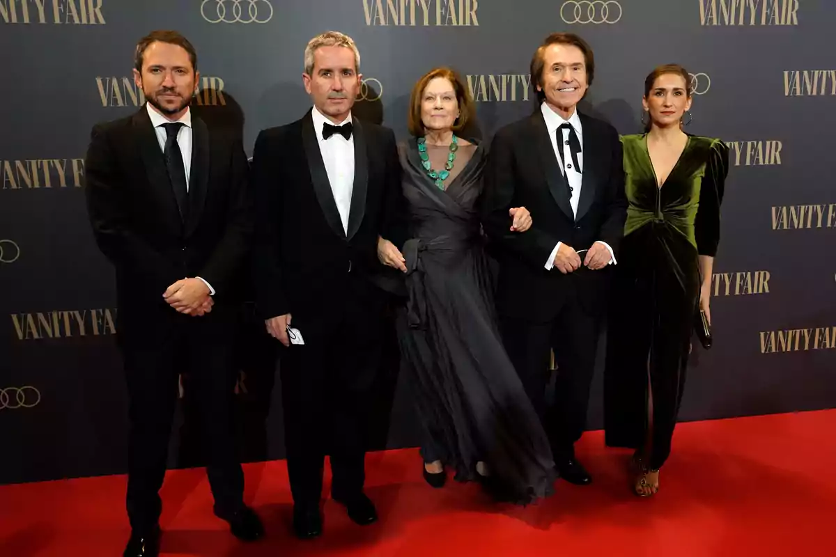 Un grupo de personas elegantemente vestidas posando en una alfombra roja frente a un fondo de Vanity Fair.