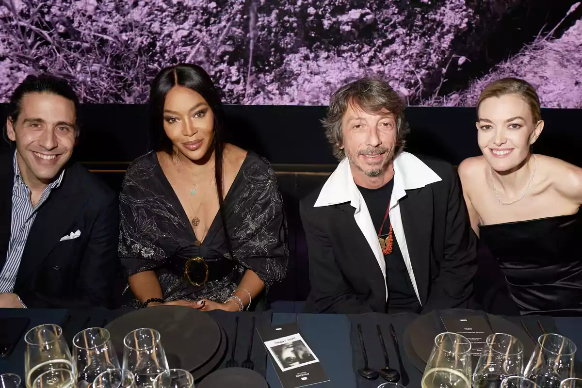 Cuatro personas sentadas en una mesa elegantemente puesta, con copas y platos, posando para la cámara en un evento social.