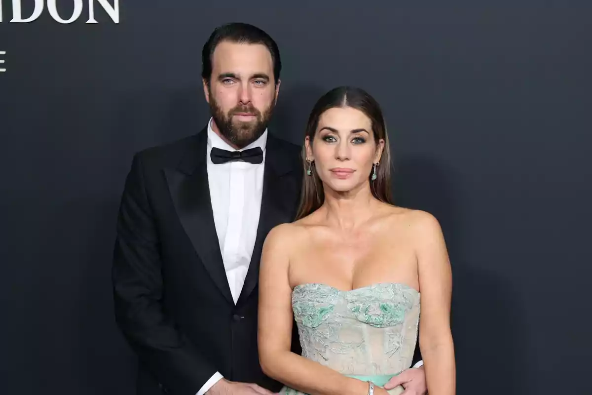 Una pareja posando en un evento formal con fondo oscuro.