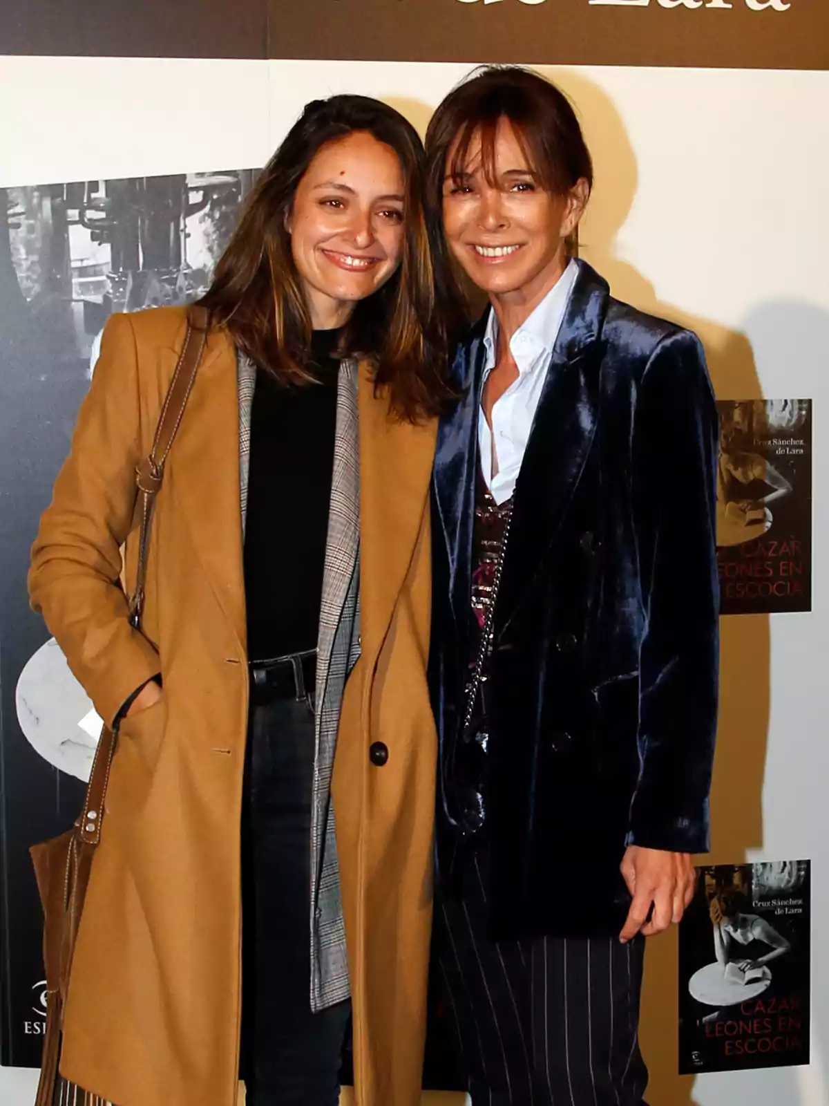 Dos mujeres sonrientes posan juntas frente a un fondo con carteles.