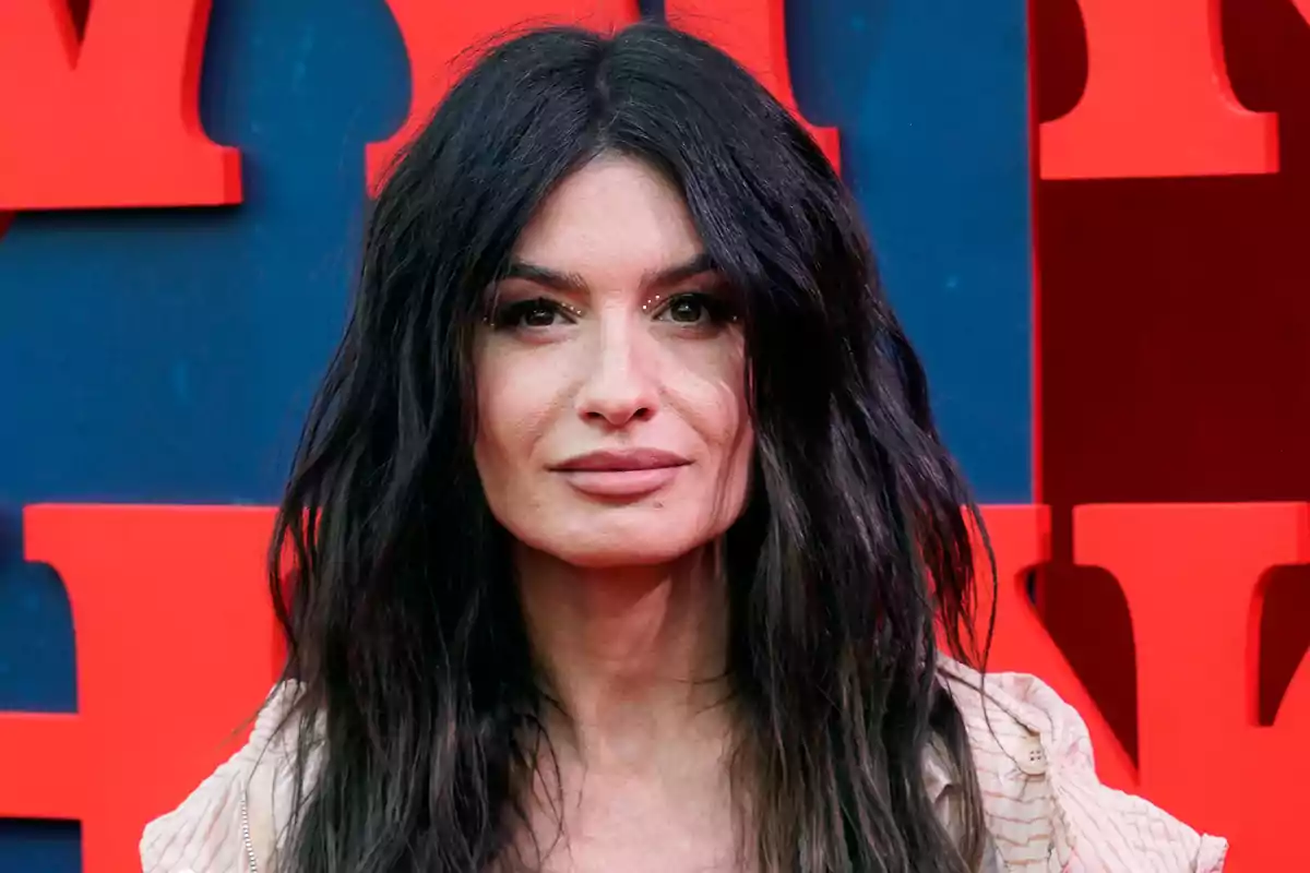 Mujer de cabello oscuro y largo frente a un fondo con letras rojas.