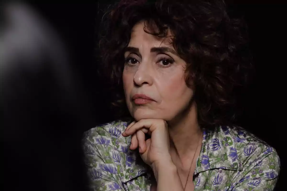 Mujer de cabello rizado con expresión pensativa y mano en el mentón, fondo oscuro. Mujer de cabello rizado con expresión pensativa y mano en el mentón, fondo oscuro.
