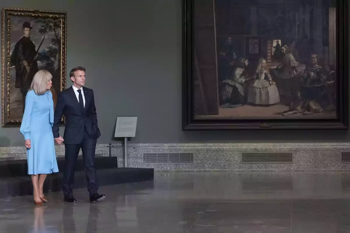 Una pareja elegantemente vestida camina de la mano en una galería de arte junto a un gran cuadro famoso y otro retrato en la pared. Una pareja elegantemente vestida camina de la mano en una galería de arte junto a un gran cuadro famoso y otro retrato en la pared.