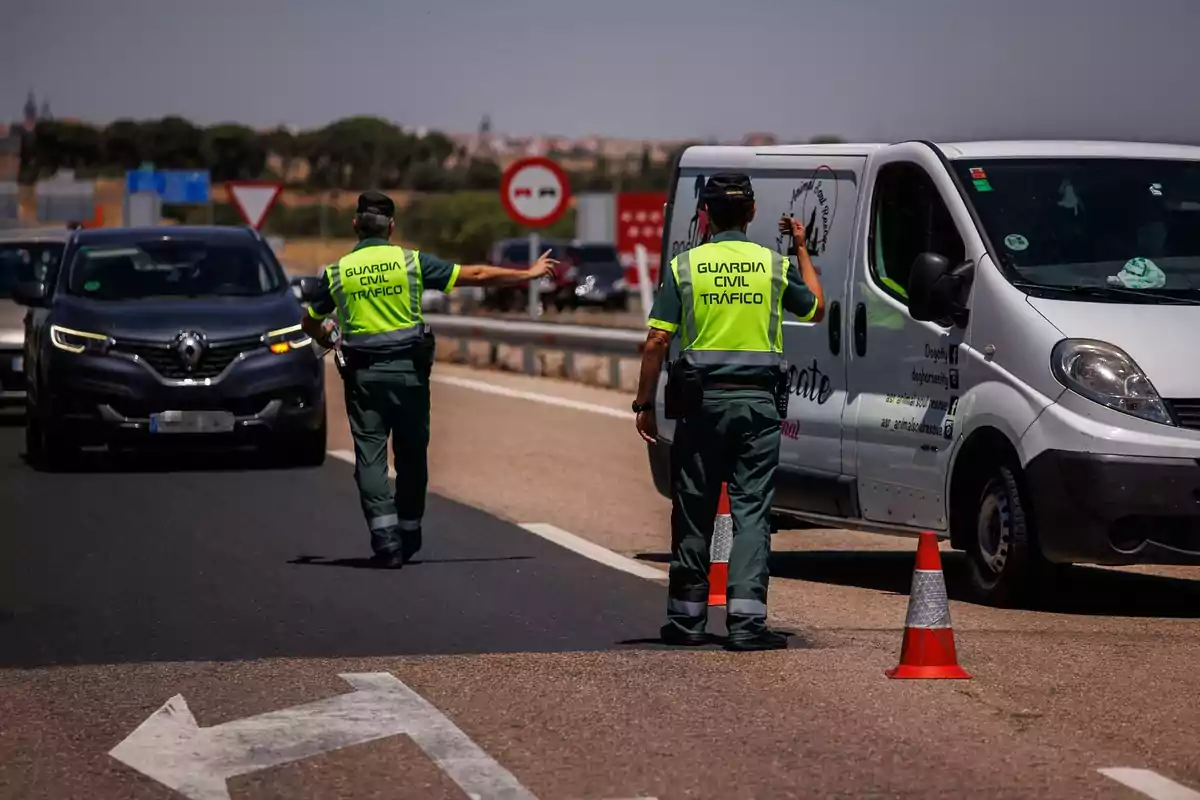 Dos agentes de la Guardia Civil de Tráfico realizan un control de carretera deteniendo vehículos en una autopista bajo un día soleado Dos agentes de la Guardia Civil de Tráfico realizan un control de carretera deteniendo vehículos en una autopista bajo un día soleado