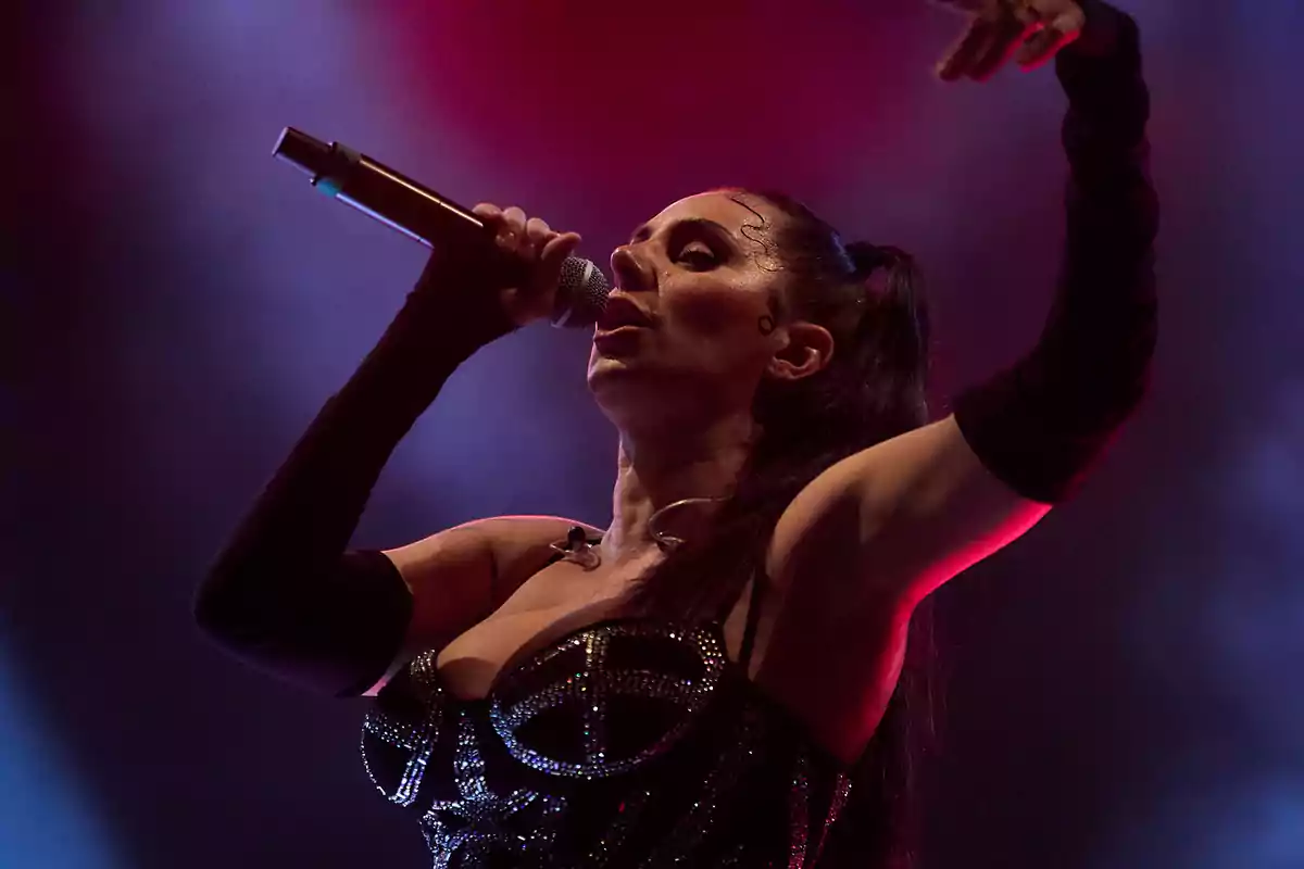 Cantante con vestuario brillante y guantes largos interpretando una canción en el escenario bajo luces de colores Cantante con vestuario brillante y guantes largos interpretando una canción en el escenario bajo luces de colores