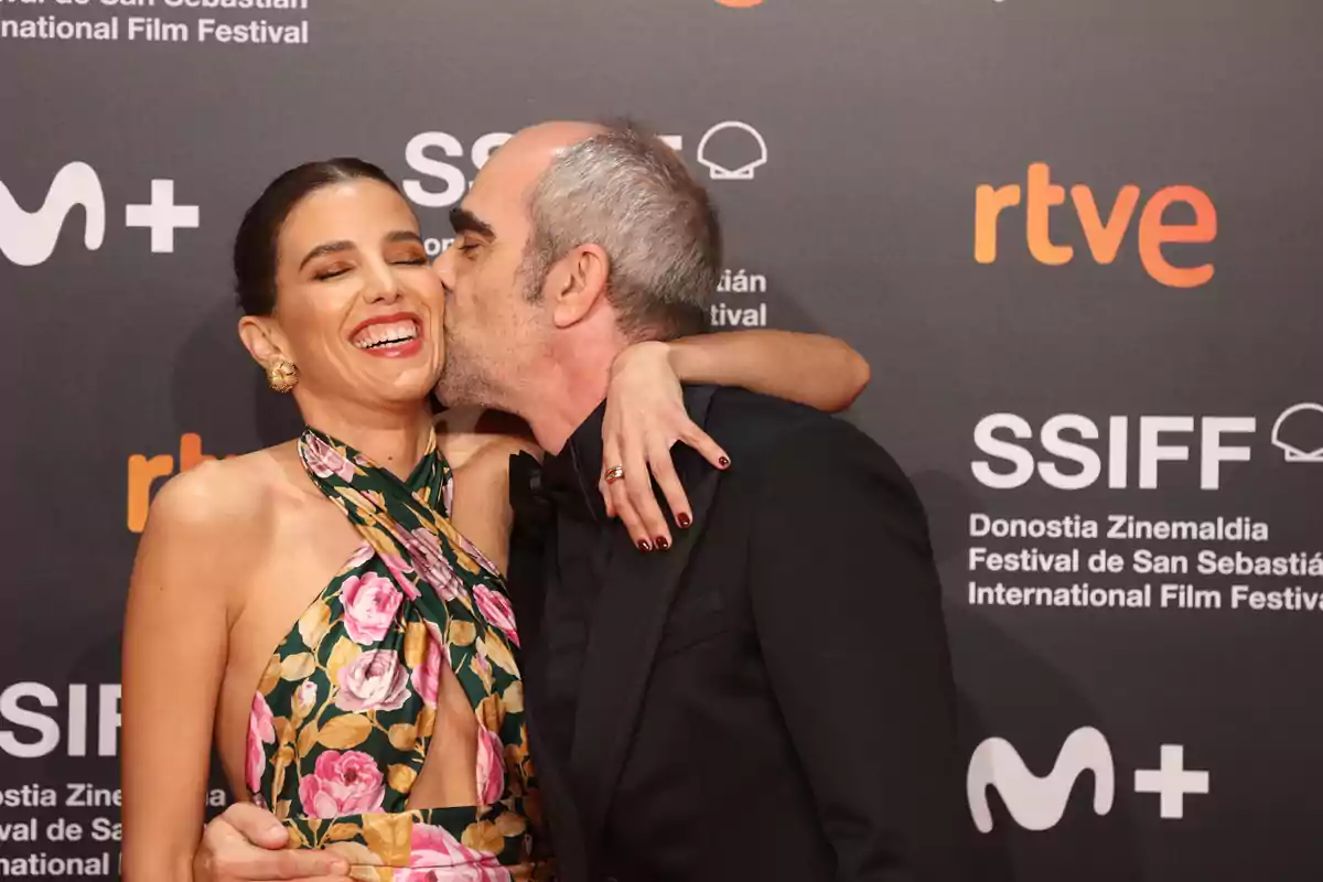 Una mujer sonriente recibe un beso en la mejilla de un hombre en un evento del Festival Internacional de Cine de San Sebastián.