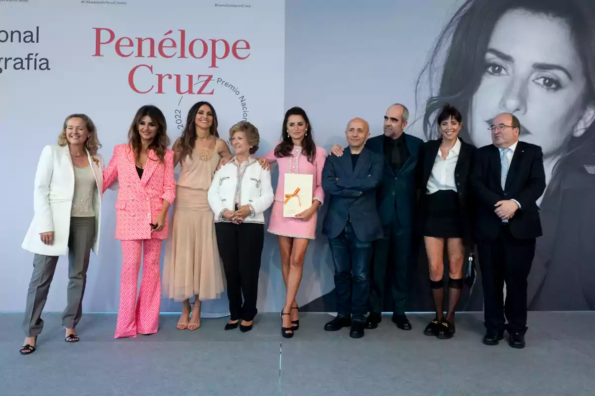 Un grupo de personas posa en un evento frente a un cartel que destaca el nombre de Penélope Cruz, con una gran fotografía en blanco y negro de ella al fondo. Un grupo de personas posa en un evento frente a un cartel que destaca el nombre de Penélope Cruz, con una gran fotografía en blanco y negro de ella al fondo.