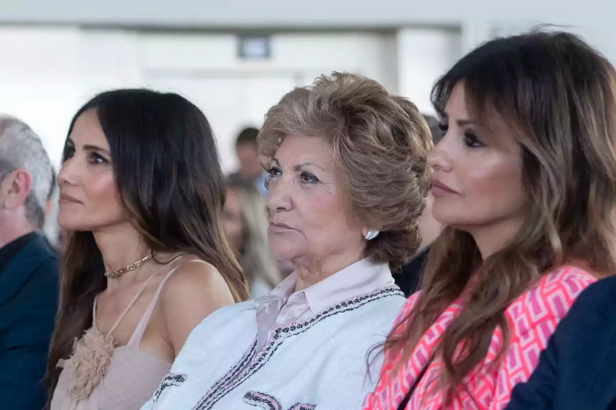 Tres mujeres sentadas en un evento, mirando hacia adelante con expresiones serias. Tres mujeres sentadas en un evento, mirando hacia adelante con expresiones serias.
