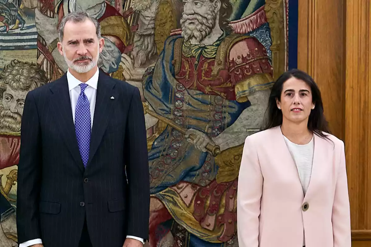 Dos personas posan frente a un tapiz colorido con figuras históricas.