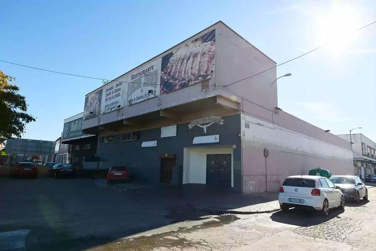Edificio de restaurante con carteles grandes en la fachada y varios coches aparcados en el exterior en un día soleado