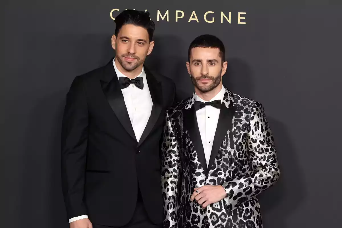 Dos hombres posan en un evento formal, uno con un esmoquin negro clásico y el otro con un esmoquin de estampado de leopardo.