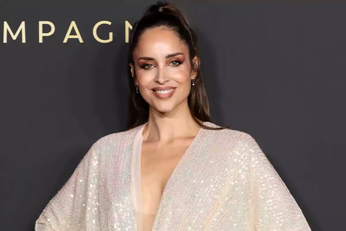 Una mujer sonriente con un vestido brillante posando frente a un fondo oscuro.