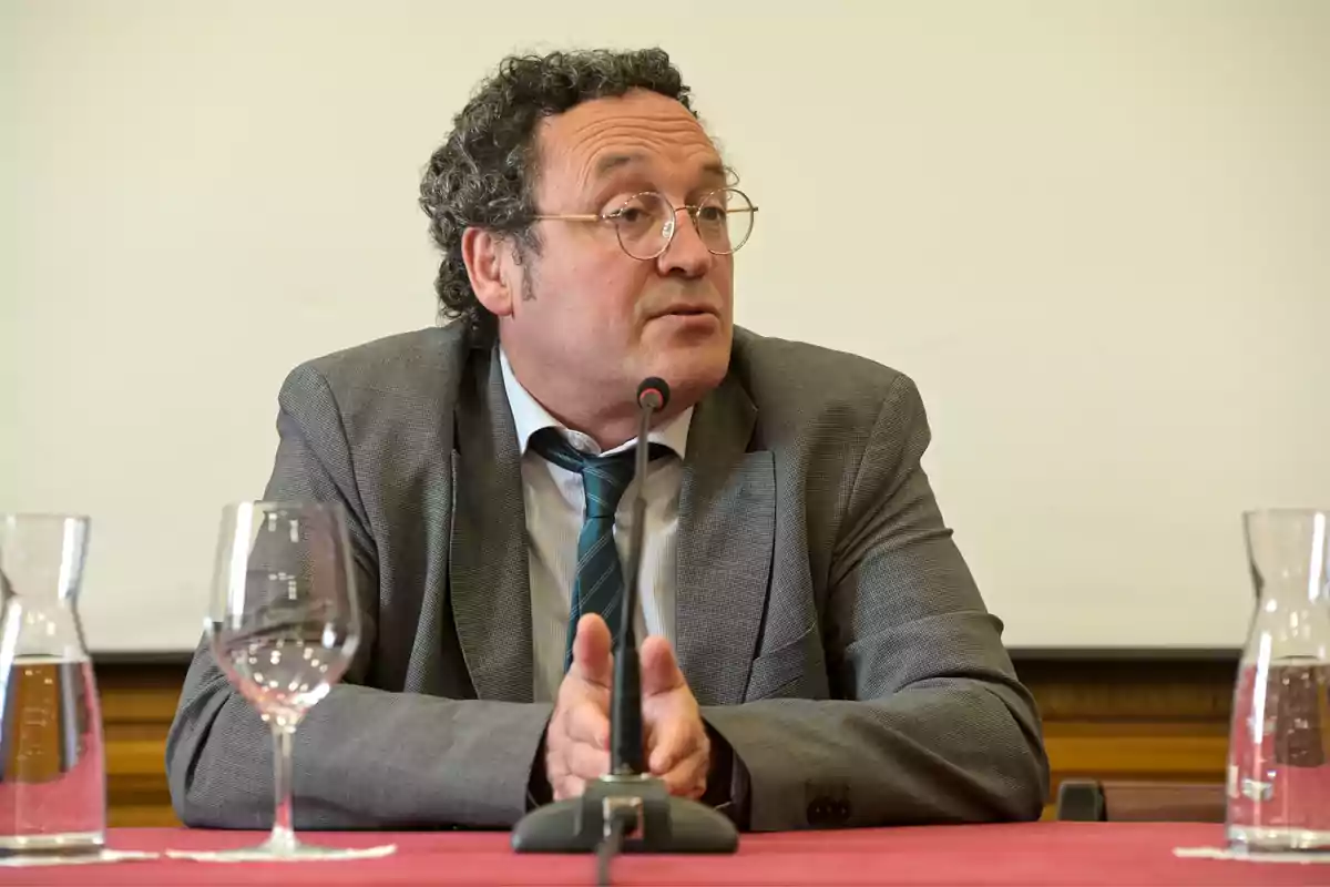 Hombre con gafas y traje hablando en un micrófono durante una conferencia.