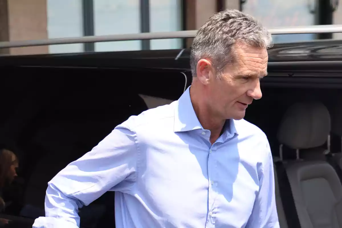 Hombre de cabello canoso con camisa azul claro saliendo de un vehículo negro en un día soleado Hombre de cabello canoso con camisa azul claro saliendo de un vehículo negro en un día soleado