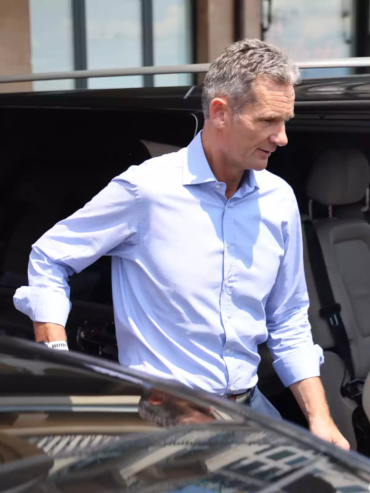 Hombre de cabello canoso con camisa azul claro saliendo de un automóvil negro en un día soleado Hombre de cabello canoso con camisa azul claro saliendo de un automóvil negro en un día soleado