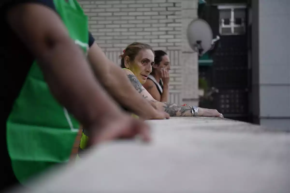 Personas apoyadas en una barandilla mirando hacia el frente con expresión pensativa.