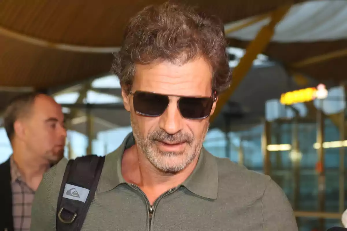 Hombre con gafas de sol y barba en un aeropuerto.