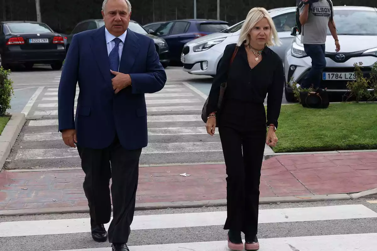 Dos personas caminando por un paso de peatones en un estacionamiento.