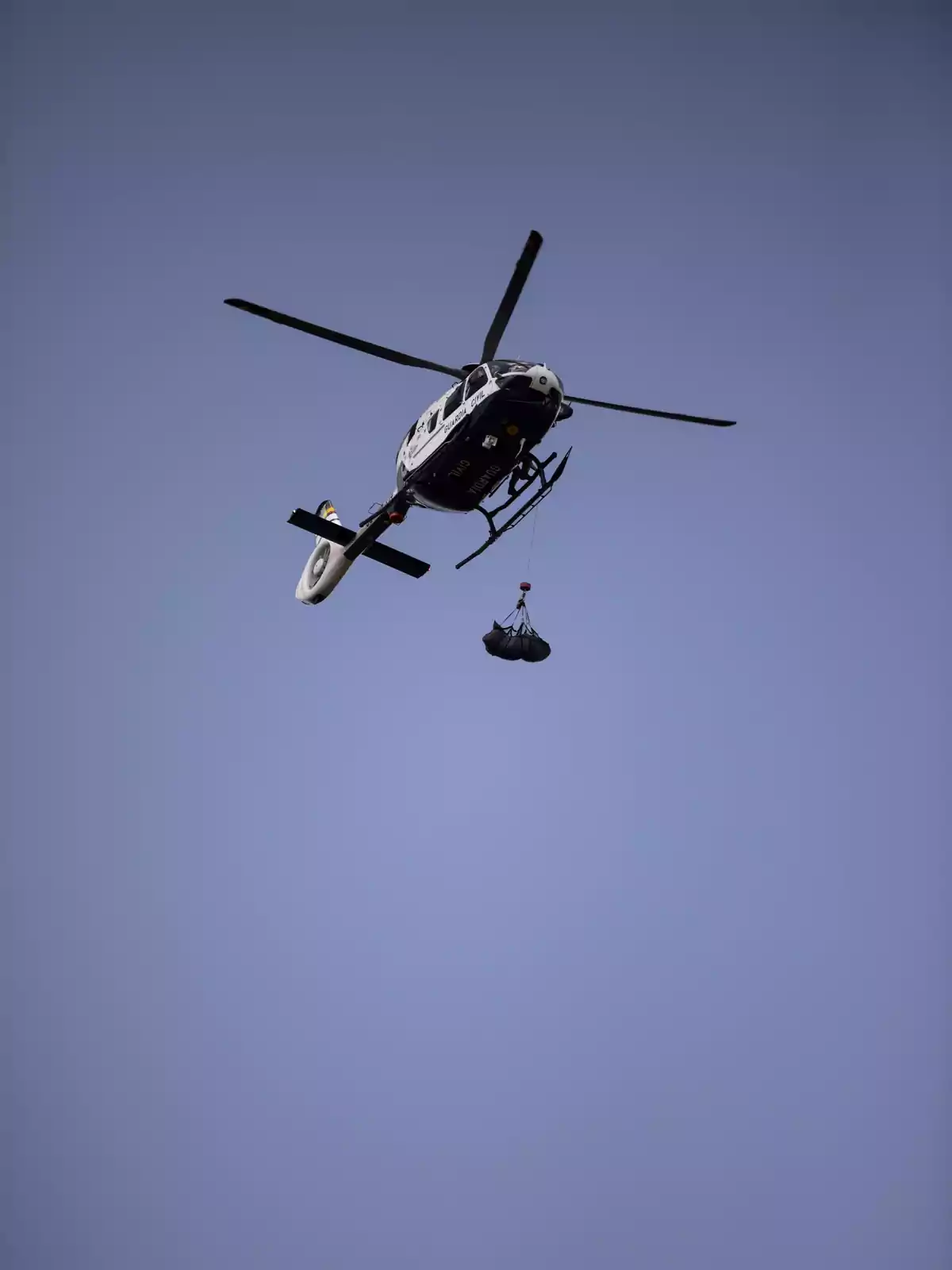 Un helicóptero volando en el cielo con una carga colgando de una cuerda.