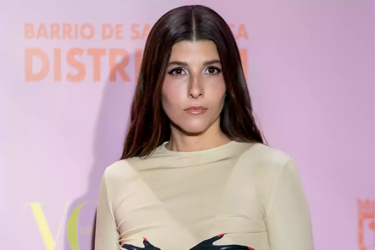 Mujer con cabello largo y liso en un evento con fondo rosa.