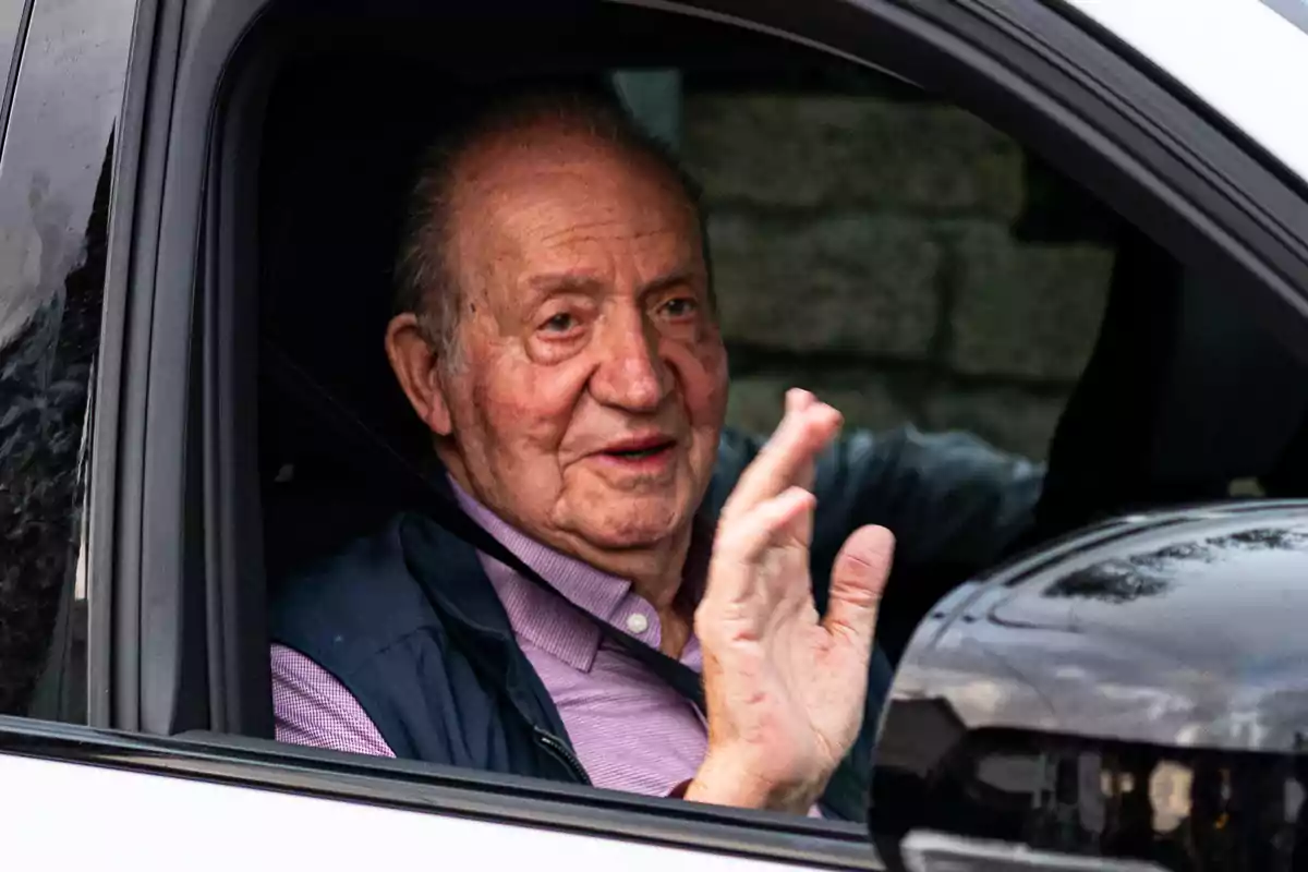 Un hombre mayor saludando desde el interior de un automóvil.