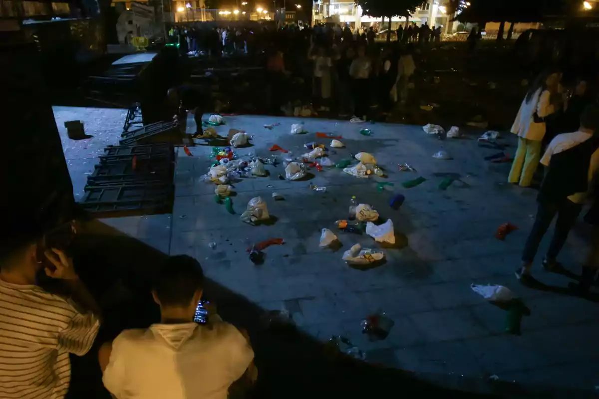 Un grupo de personas se encuentra en una plaza por la noche, con basura esparcida por el suelo.