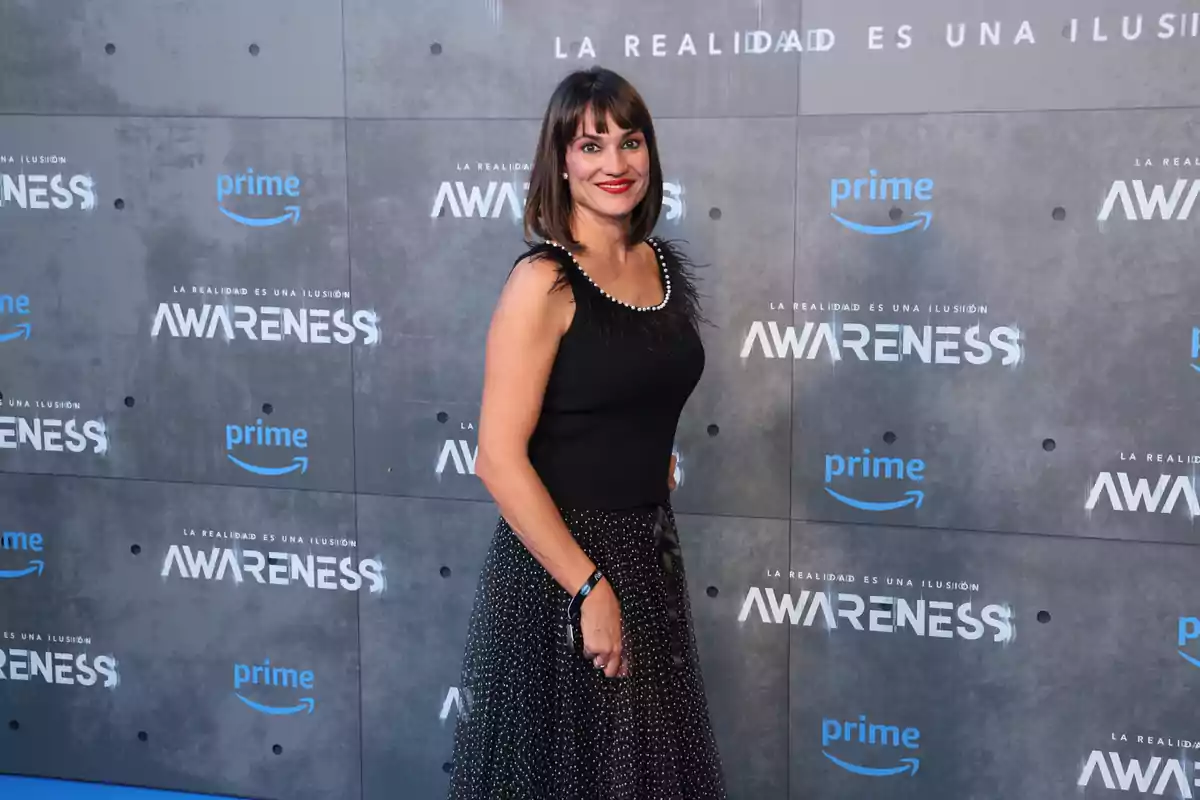 Una mujer posando en un evento de Amazon Prime Video con el fondo promocional de la serie 