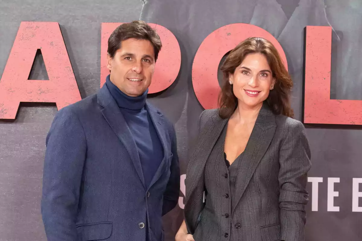 Dos personas posan juntas frente a un fondo con letras grandes y rojas.