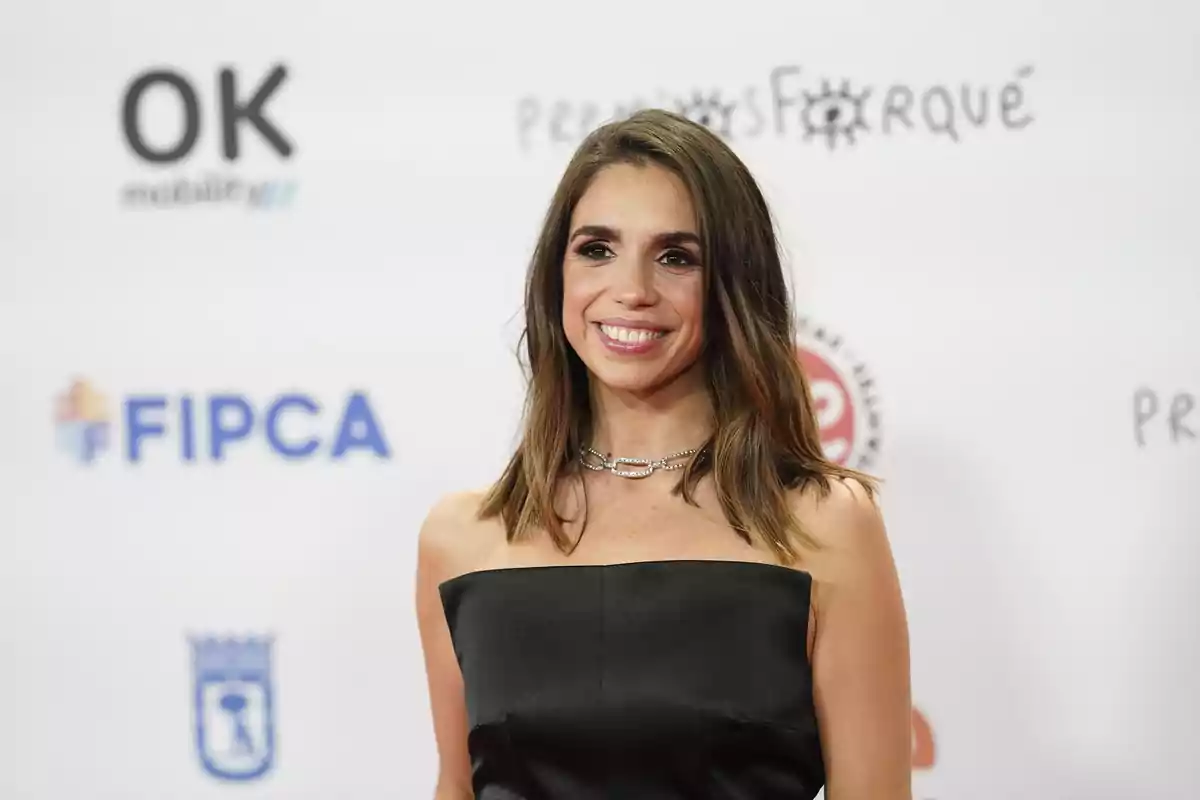 Una persona sonriendo en un evento con fondo de logotipos. Una persona sonriendo en un evento con fondo de logotipos.