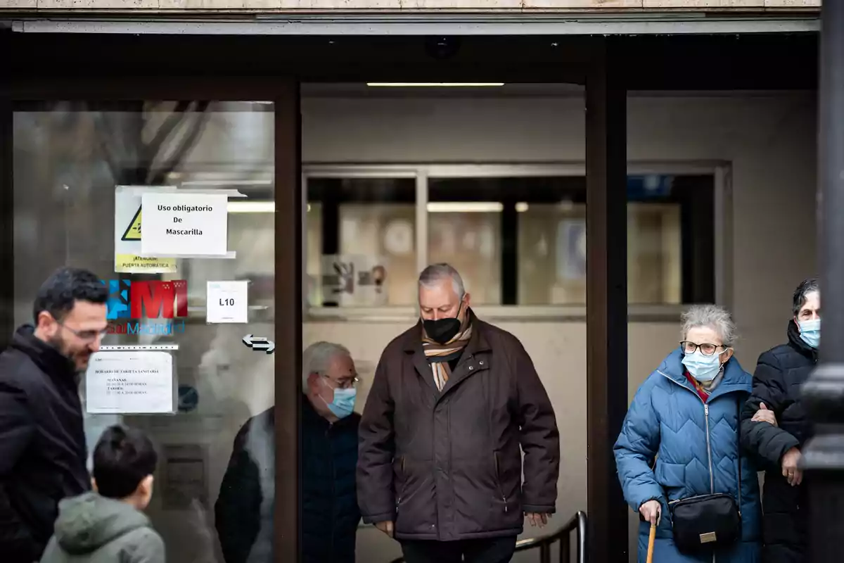 Personas con mascarillas saliendo de un edificio con un cartel que indica el uso obligatorio de mascarilla.