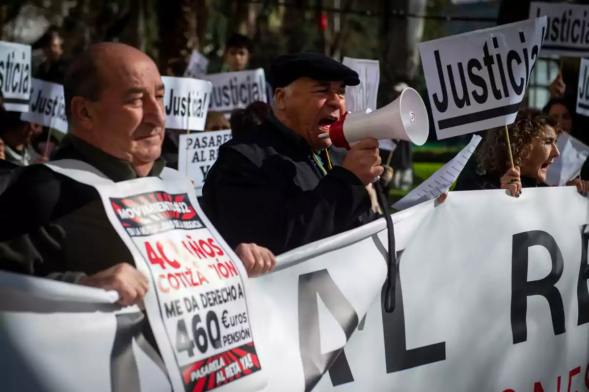 Un grupo de personas participa en una manifestación sosteniendo pancartas que piden justicia; un hombre usa un megáfono para hablar.