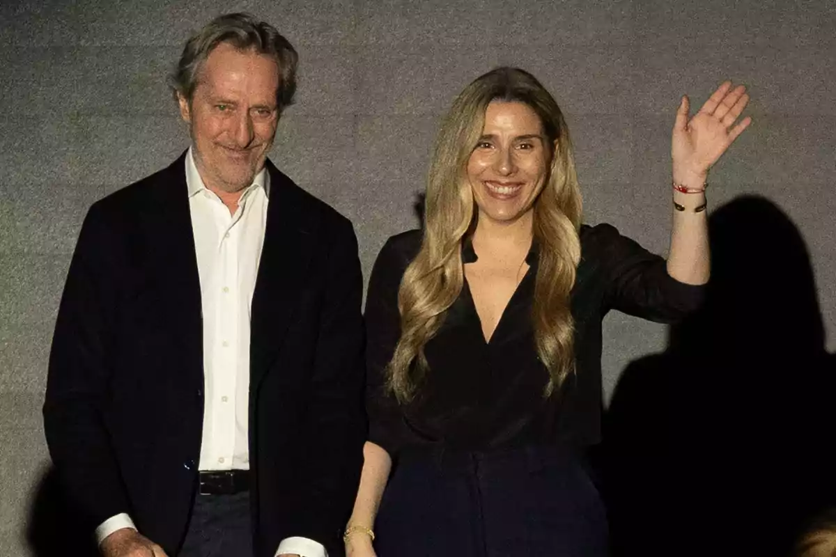 Dos personas posan juntas, una de ellas saluda con la mano levantada. Dos personas posan juntas, una de ellas saluda con la mano levantada.