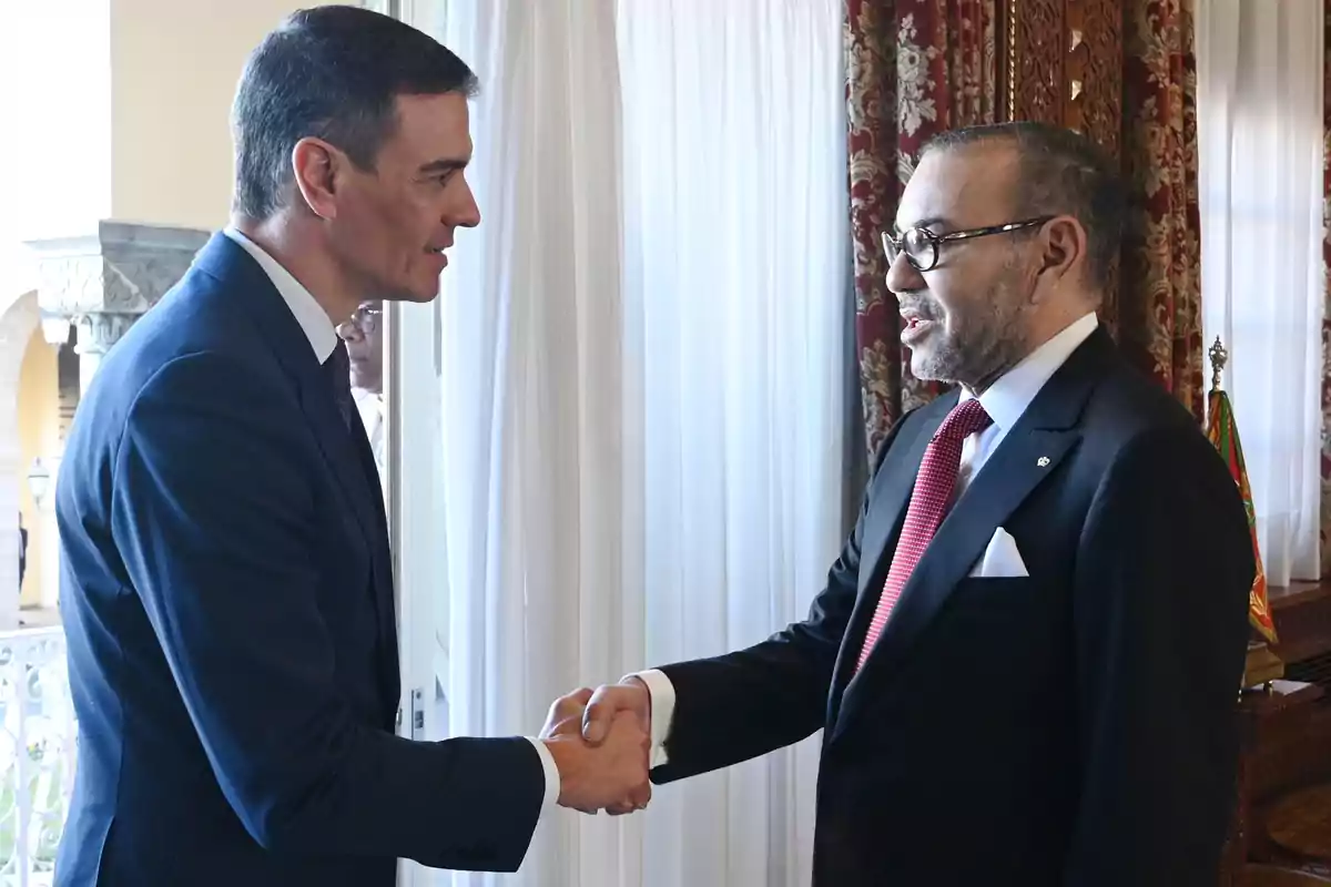 Dos hombres de traje estrechando manos en una reunión formal.