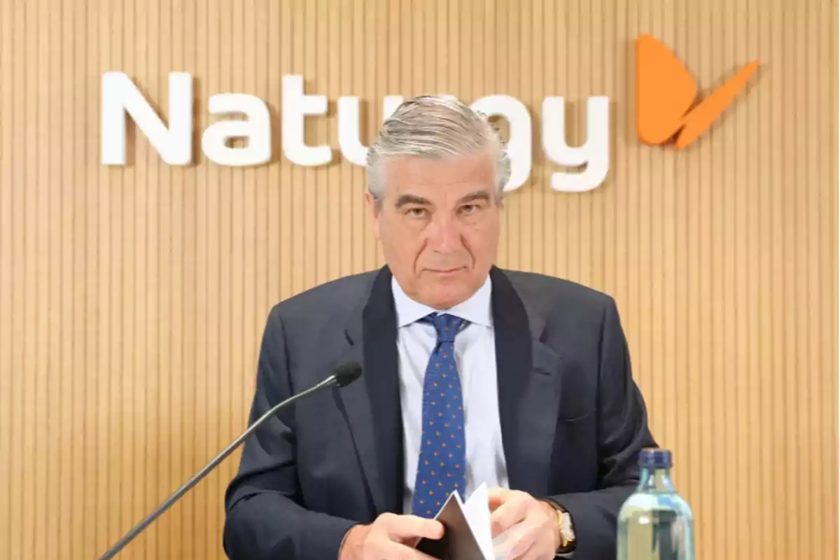 Hombre de traje y corbata azul en una conferencia de prensa con el logo de Naturgy en el fondo.