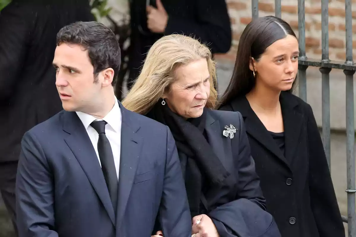 Tres personas vestidas de negro están de pie juntas en un evento formal al aire libre.