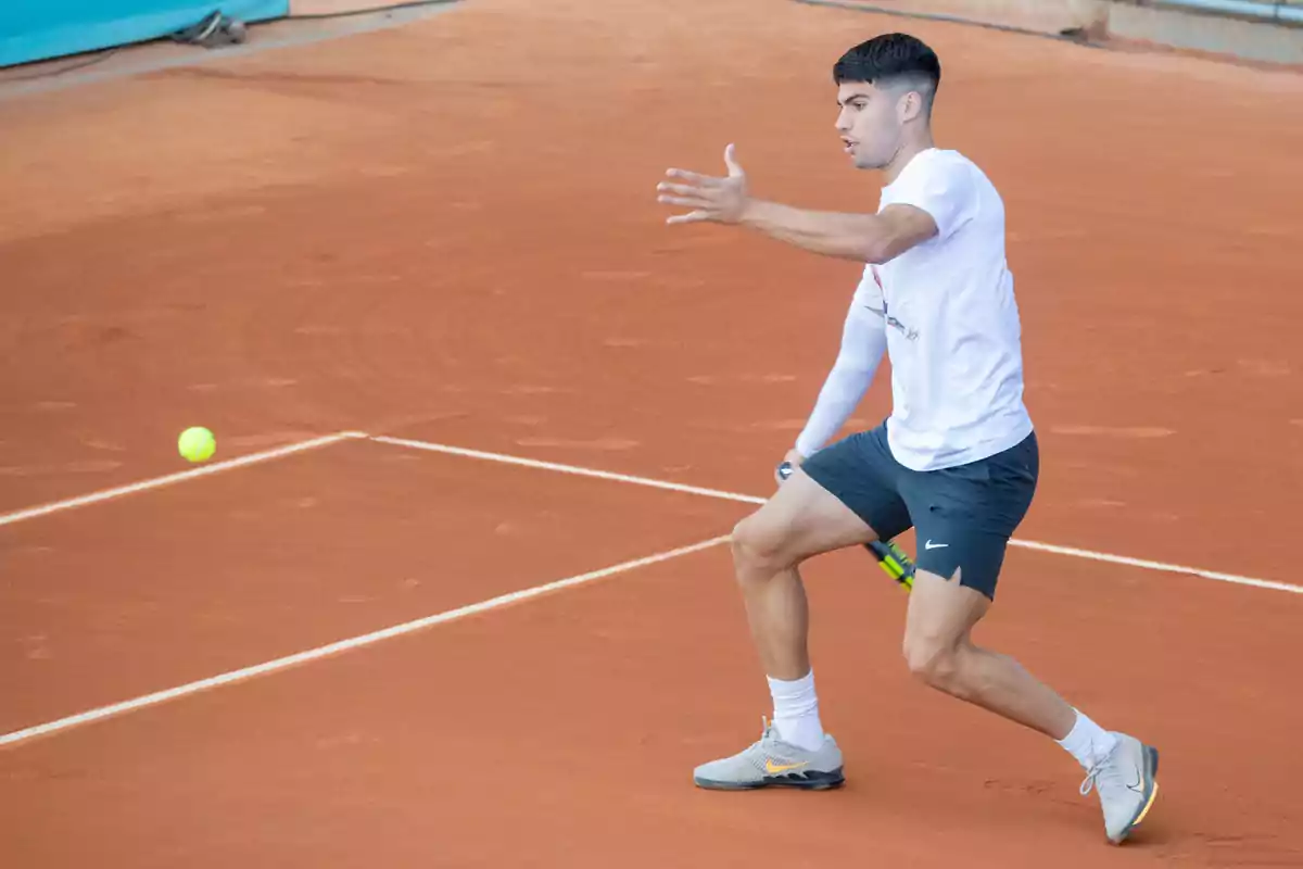 Un jugador de tenis en una cancha de arcilla preparándose para golpear una pelota con su raqueta.