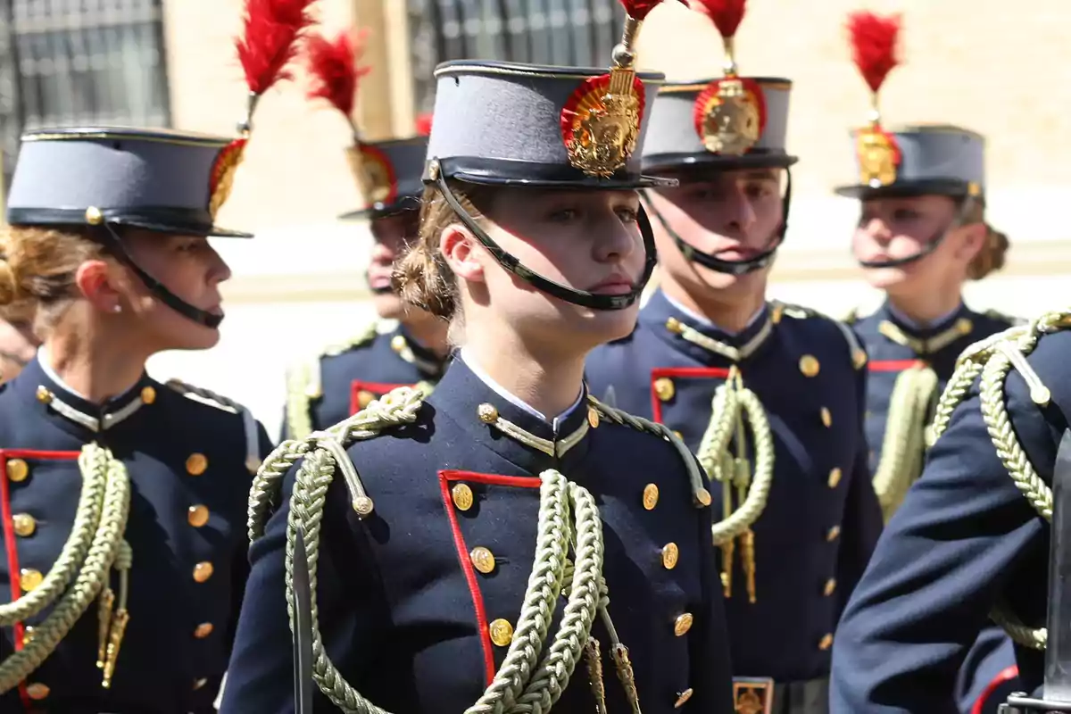 Cadetes en uniforme militar con sombreros adornados con plumas rojas durante una ceremonia.