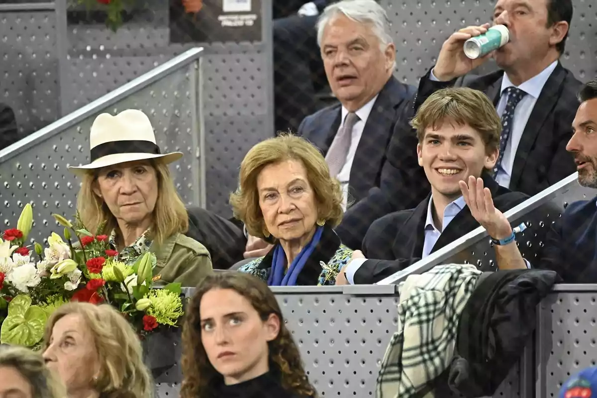 Un grupo de personas sentadas en un evento deportivo, algunas sostienen flores y otras parecen conversar y disfrutar del ambiente. Un grupo de personas sentadas en un evento deportivo, algunas sostienen flores y otras parecen conversar y disfrutar del ambiente.