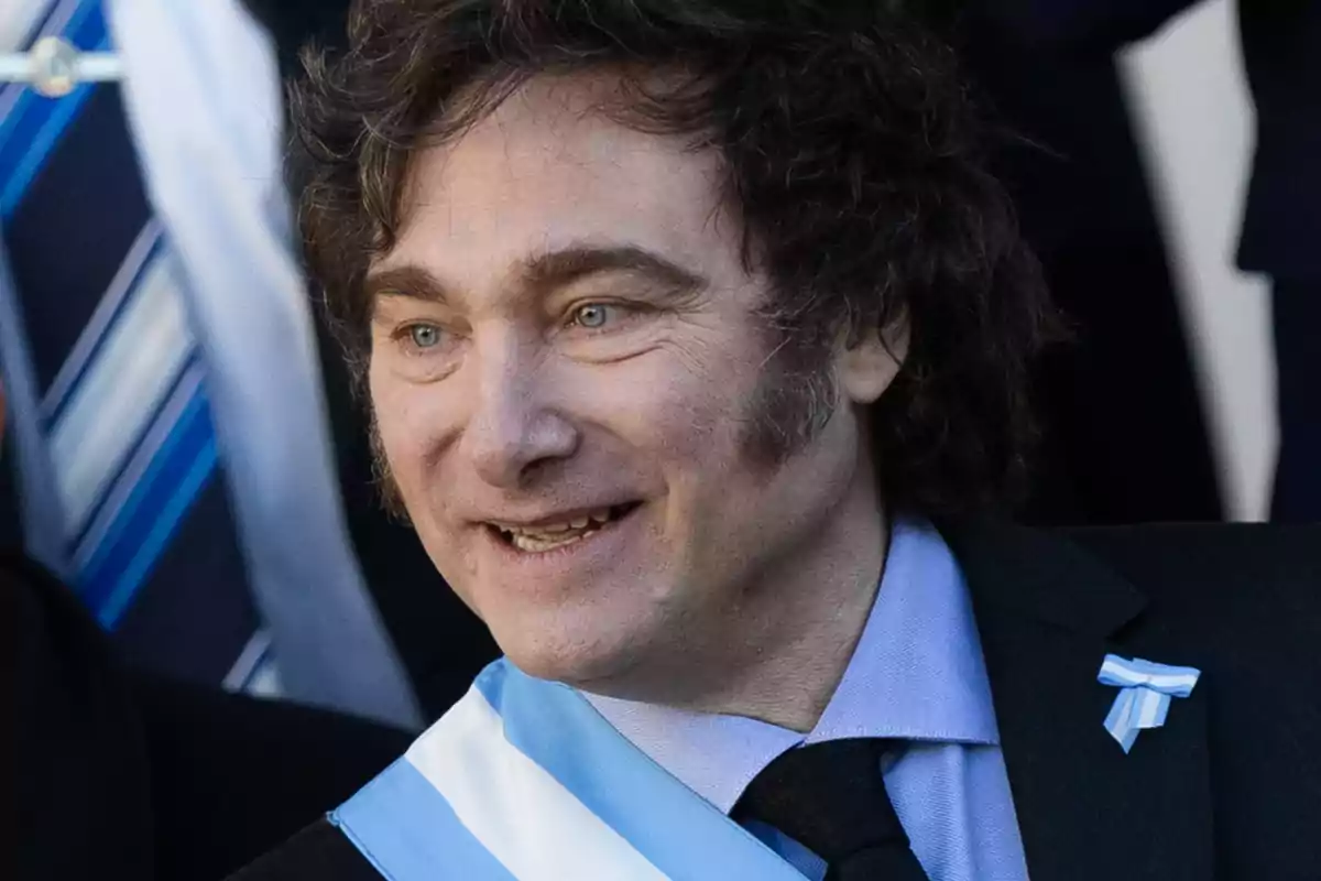 Hombre con cabello rizado y ojos claros, vistiendo una banda y un traje formal con corbata negra.