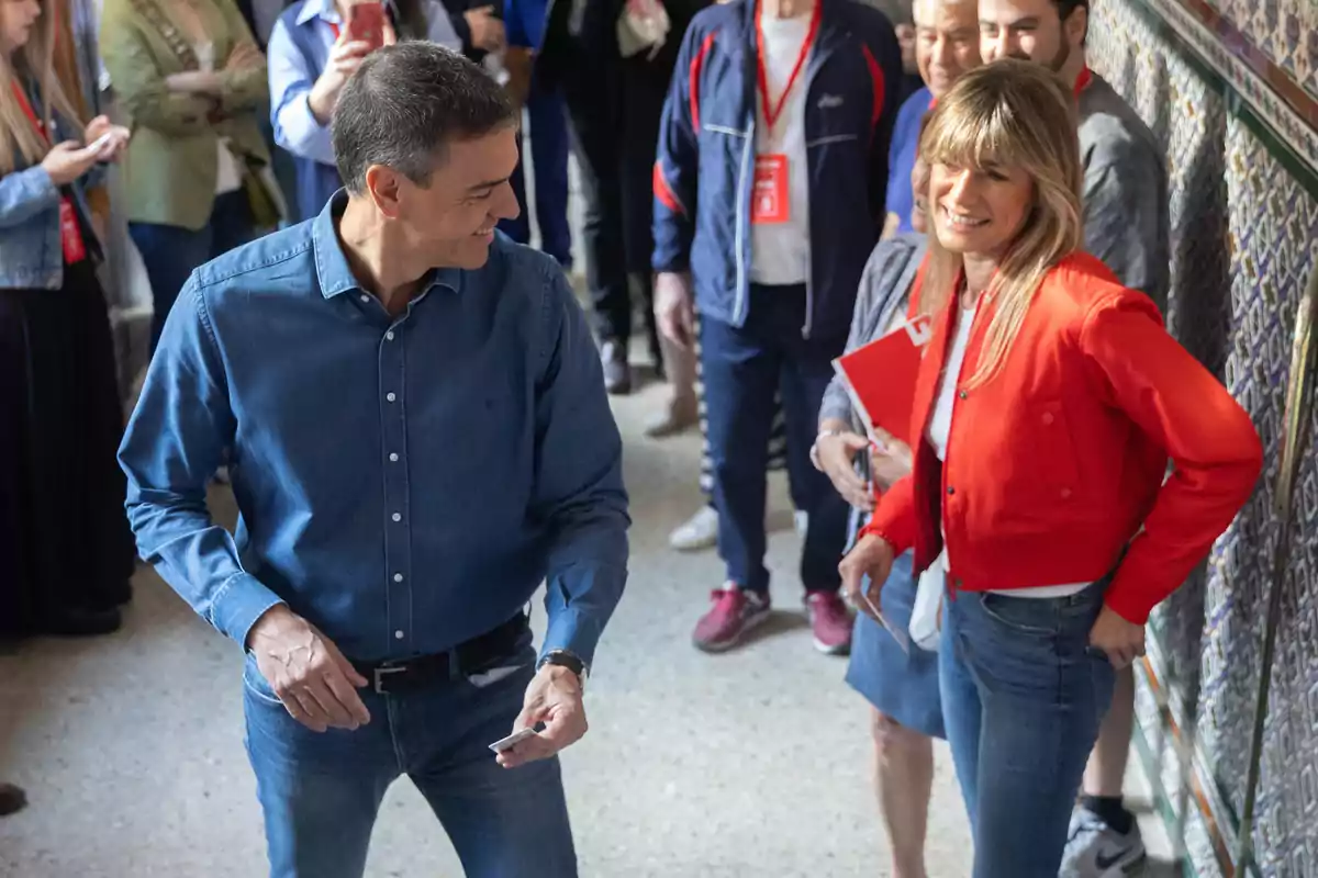 Un grupo de personas sonríe y conversa en un espacio interior decorado con azulejos, destacando dos personas en primer plano, una con camisa azul y otra con chaqueta roja.