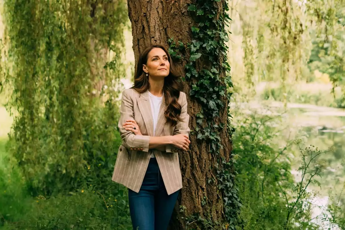 Mujer de pie junto a un árbol en un entorno natural con vegetación abundante.