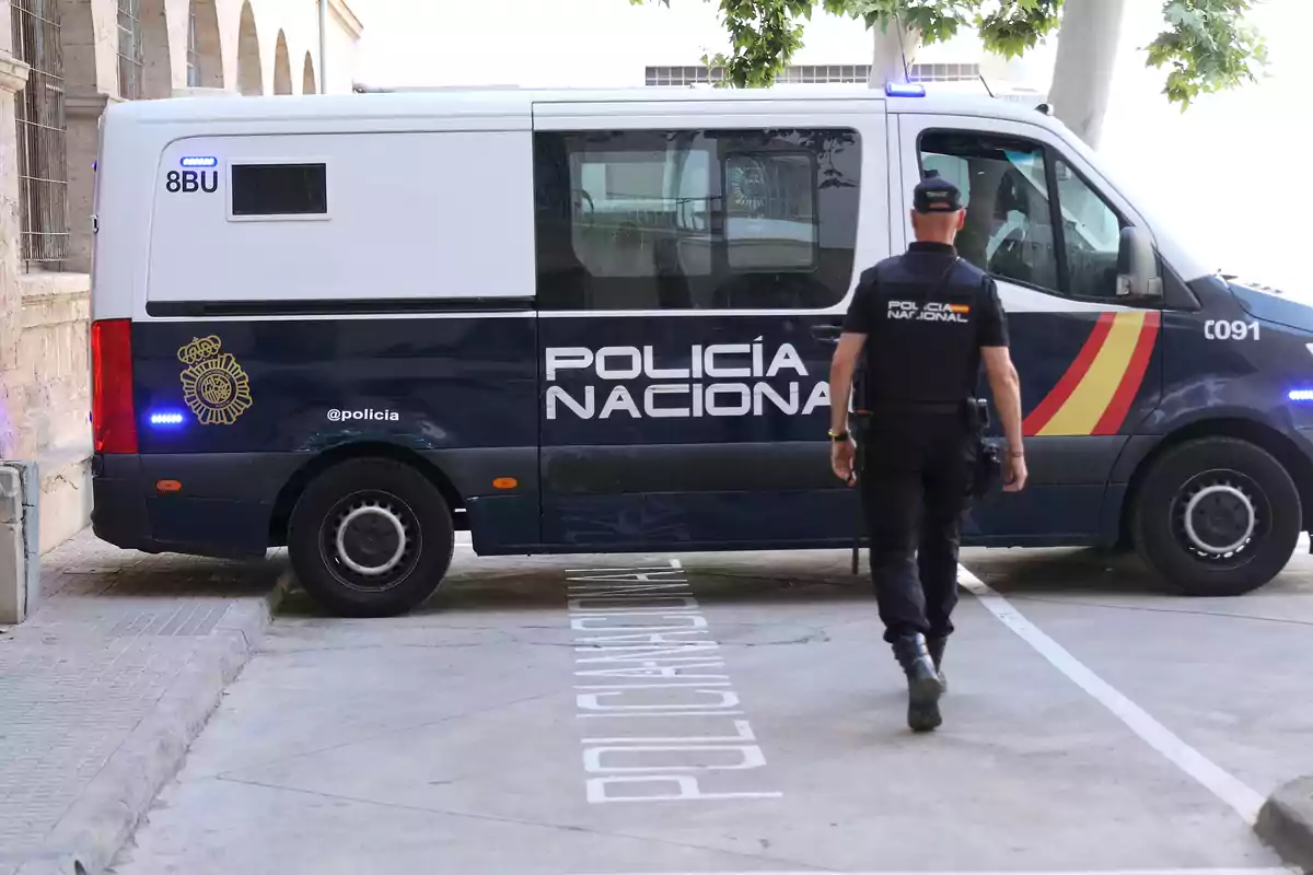 Un oficial de la Policía Nacional camina hacia una furgoneta policial estacionada en una zona designada.