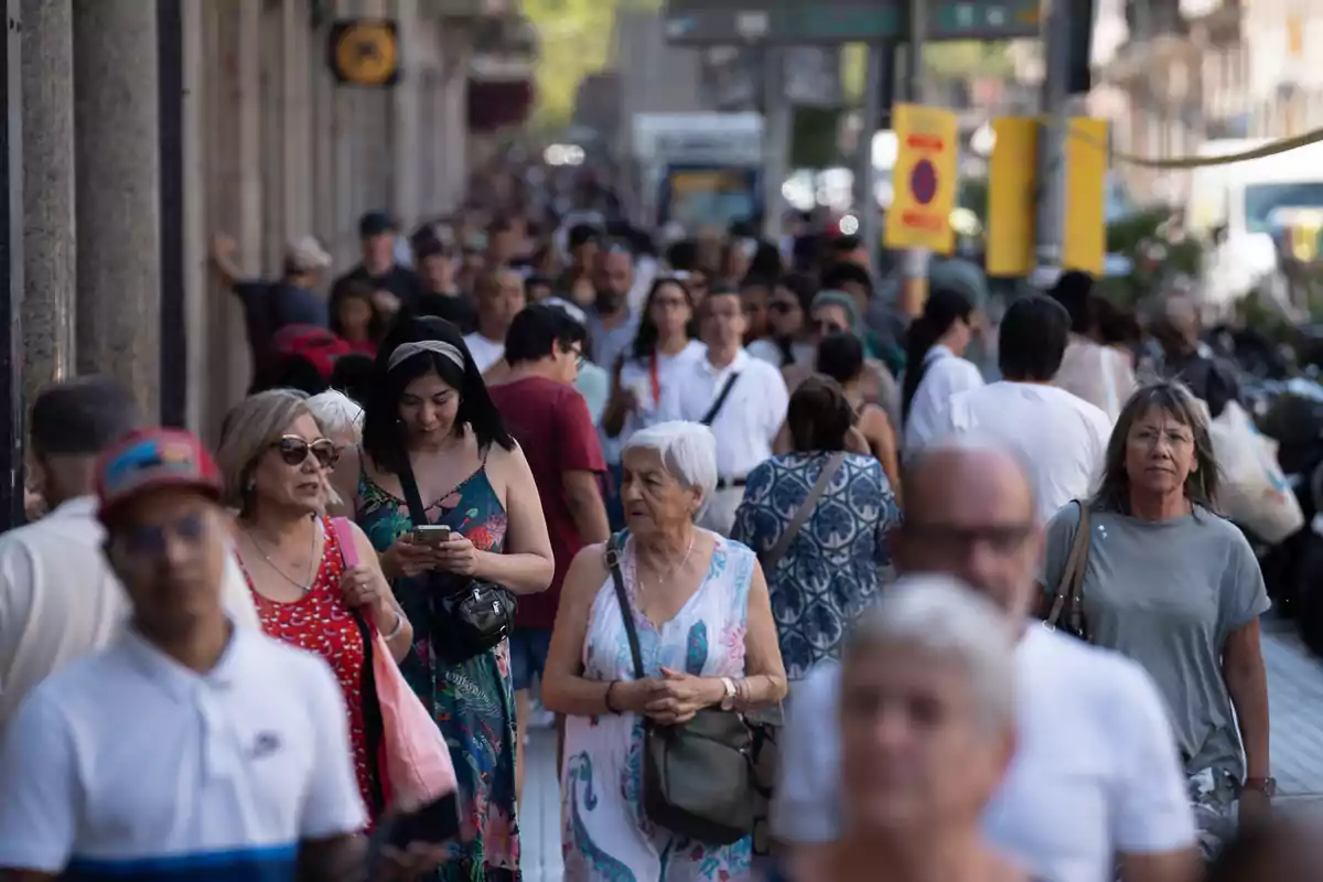 Una multitud de personas camina por una acera concurrida en un día soleado.