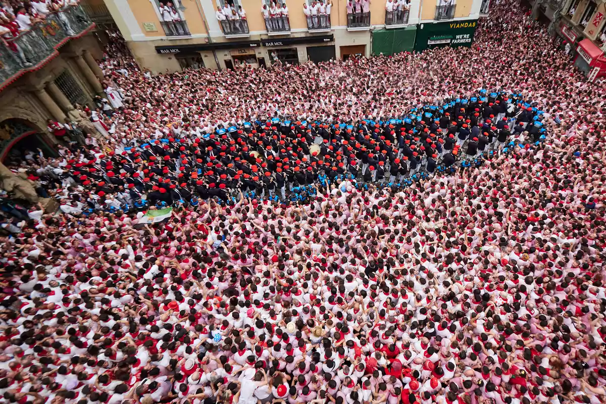 Una multitud de personas vestidas de blanco y rojo se congrega en una calle durante un evento festivo.