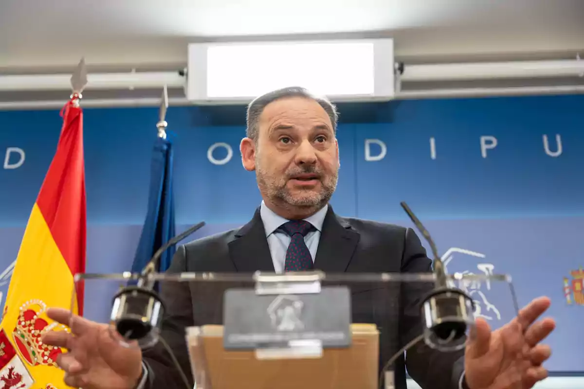 Un hombre en un podio con banderas de España y un fondo azul.