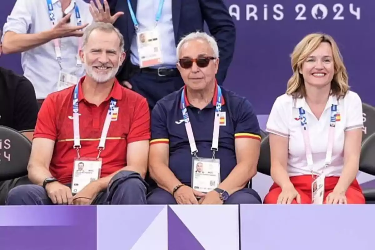 Tres personas sentadas, dos hombres y una mujer, con credenciales colgadas del cuello, en un evento relacionado con París 2024.