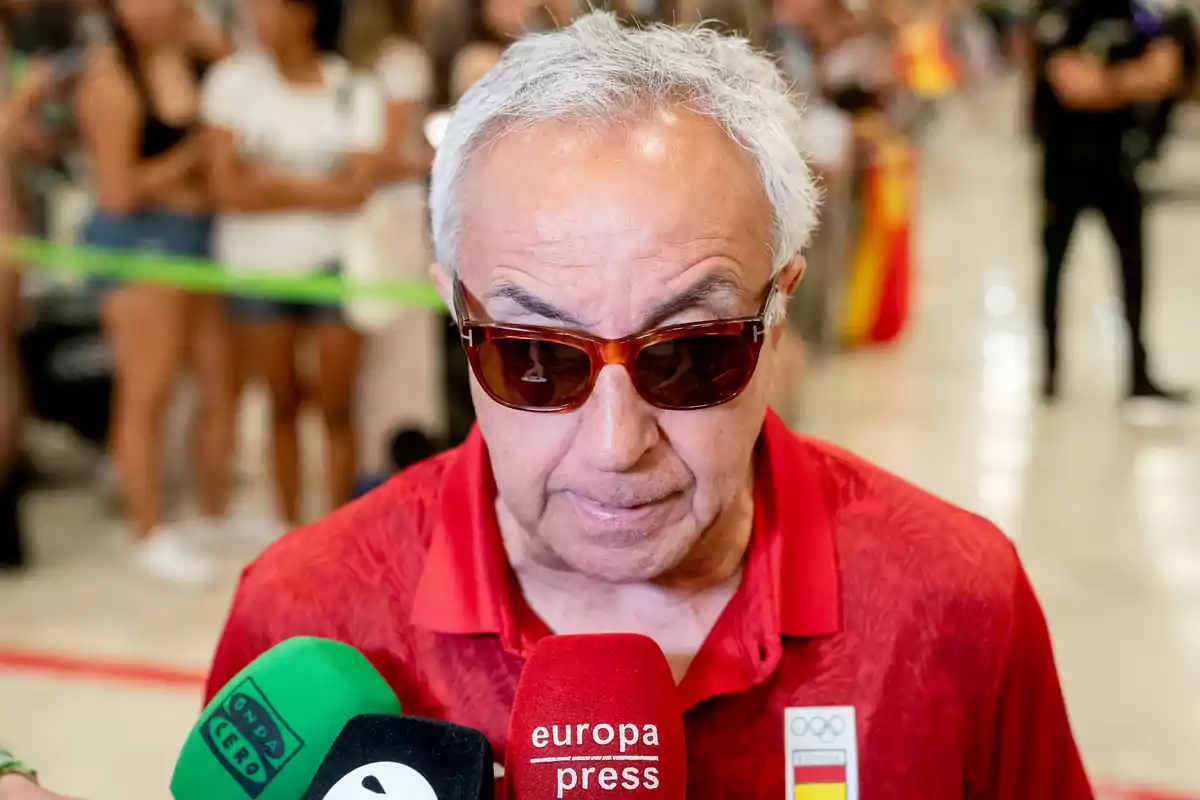 Un hombre con gafas de sol y camisa roja es entrevistado por varios medios de comunicación.